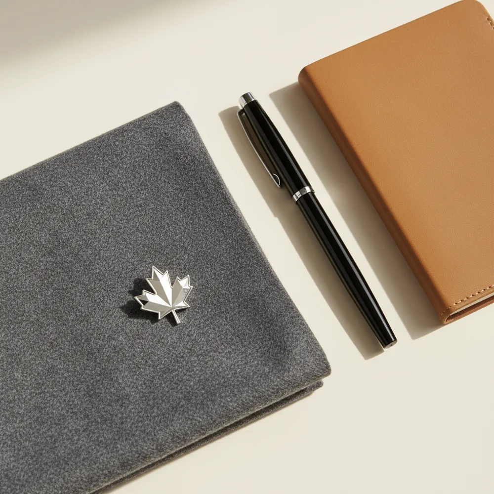 Maple leaf pin on grey fabric beside a pen and notebook